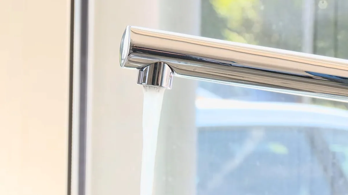 Chrome kitchen faucet with a steady stream of water in front of a bright window