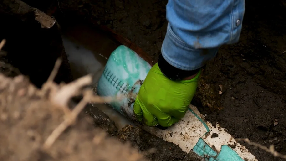 Gloved hand guiding a teal resin-coated liner into place inside a dirt excavation