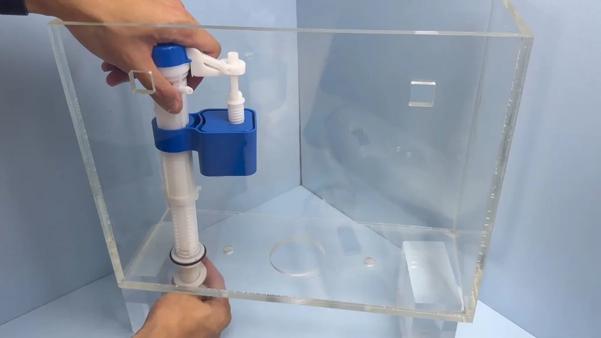 Hands setting a white and blue fill valve into a clear acrylic toilet tank model