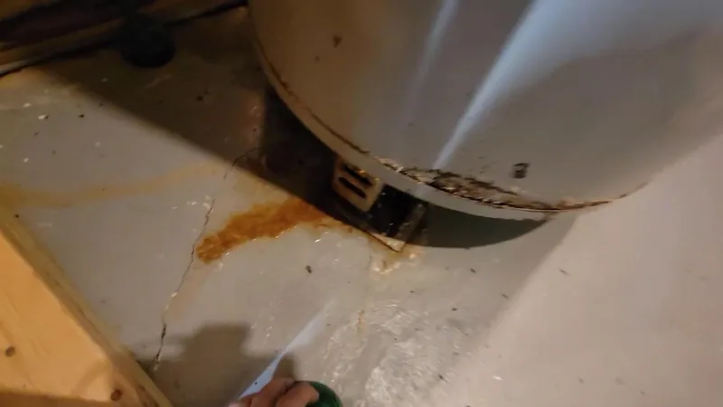 Rust-colored stain and a crack in the floor beneath the base of a white tank water heater