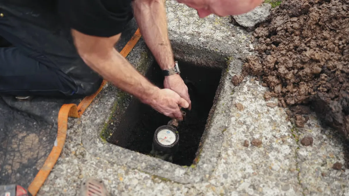 Technician reaching into an in-ground concrete box to check a water meter dial
