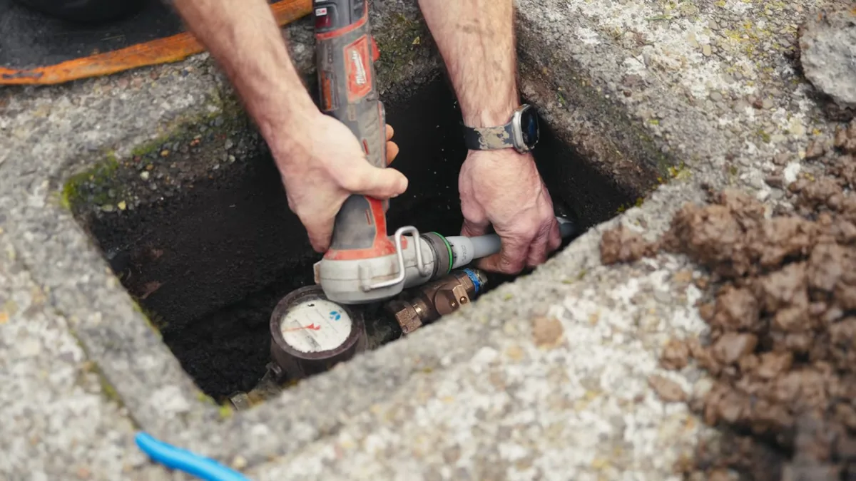 Technician working on a pipe fitting beside a water meter inside an in-ground concrete box